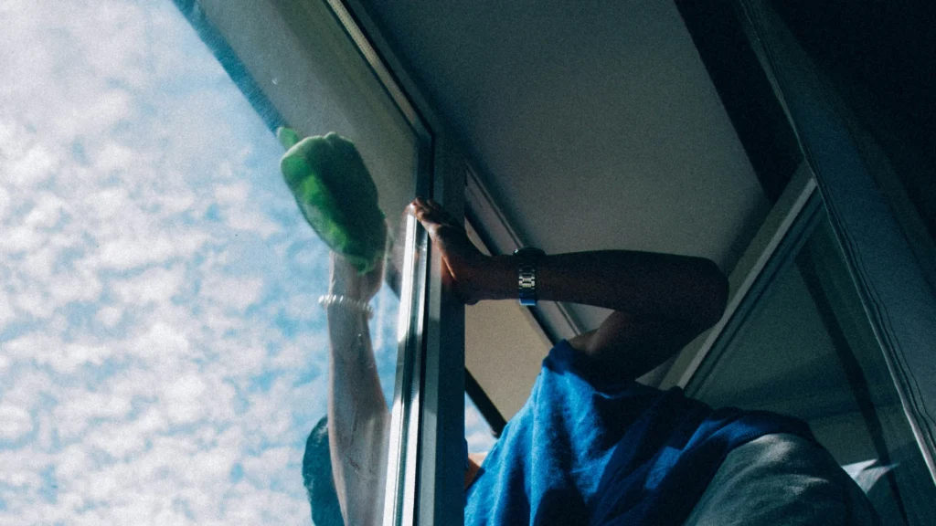 Mężczyzna myjący nowoczesne okna PCV przy użyciu gąbki na tle nieba